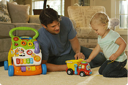Parent with child playing with Drop & Go Dump Truck and Sit-to-Stand Learning Walker from VTech